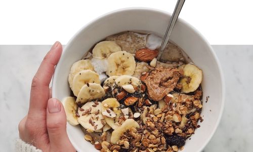 a hand holding a bowl of granola topped with banana slices and nuts health coaching option