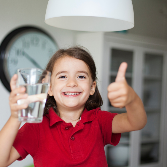 A little girl holding up a glass of water and giving a thumbs up.