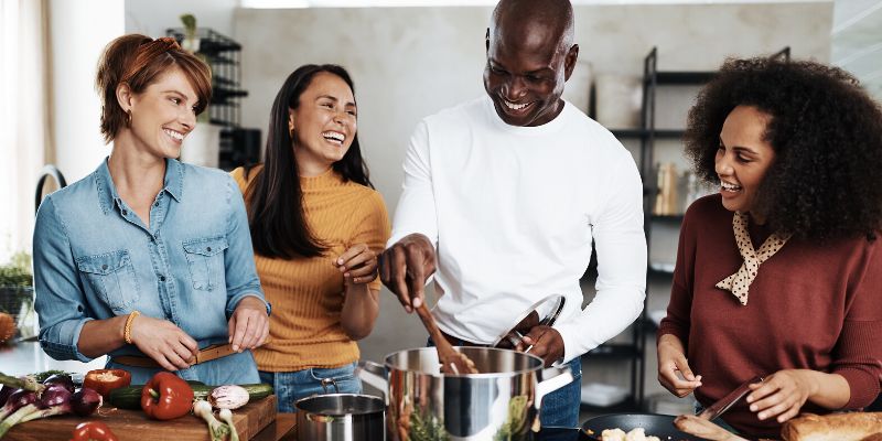 A group of people cooking healthy food in the kitchen while laughing and talking to each other using the guidance of a health coach 